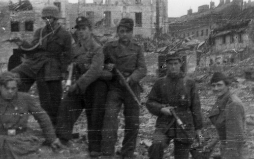 Sześcioosobowa grupa powstańców warszawskich na tle ruin miasta.